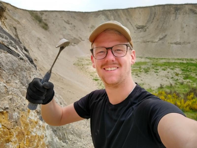 Billedet viser en smilende mand med en fossilhammer i hånden