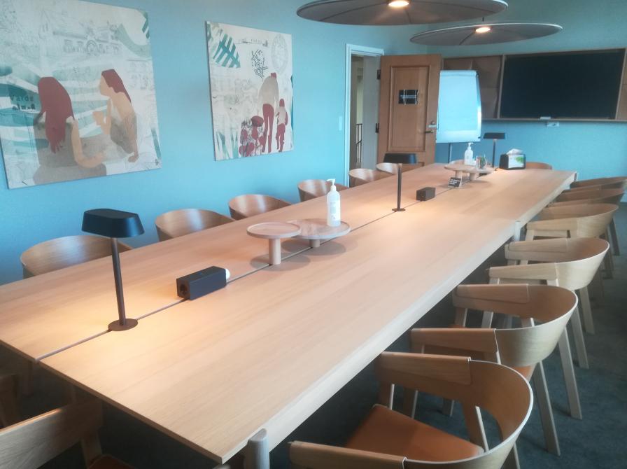 Billedet viser et langt mødebord i lyst træ med tilhørende stole